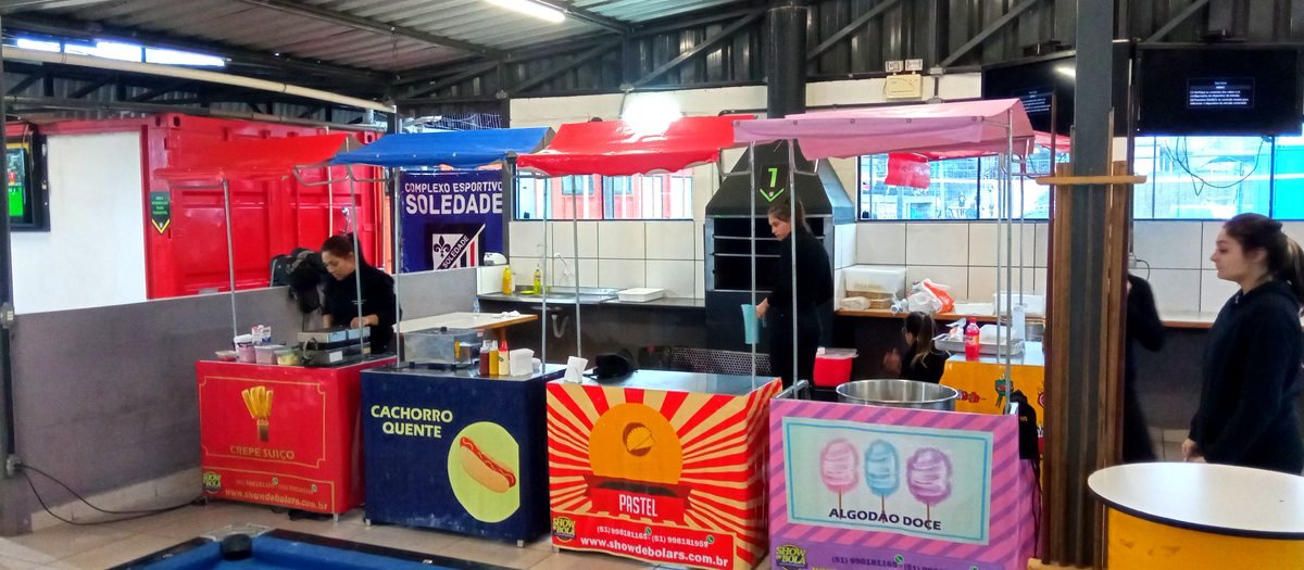 Barraquinhas de crepe, cachorro-quente, pastel e algodão doce montadas lado a lado com as atendentes